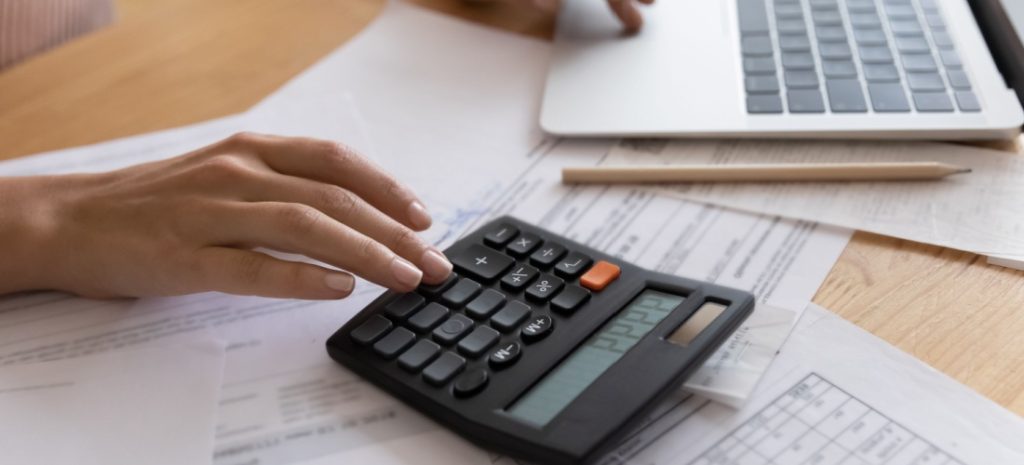 Manos de una persona manejando una calculadora, un ordenador y varias facturas de luz.